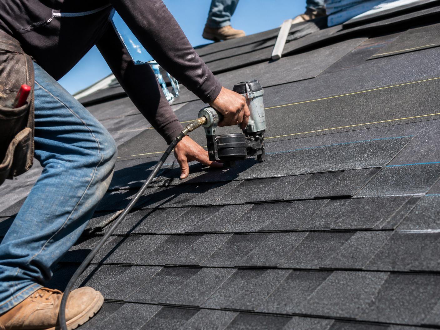 Close-up of a roofer using a nail gun to install architectural asphalt shingles
